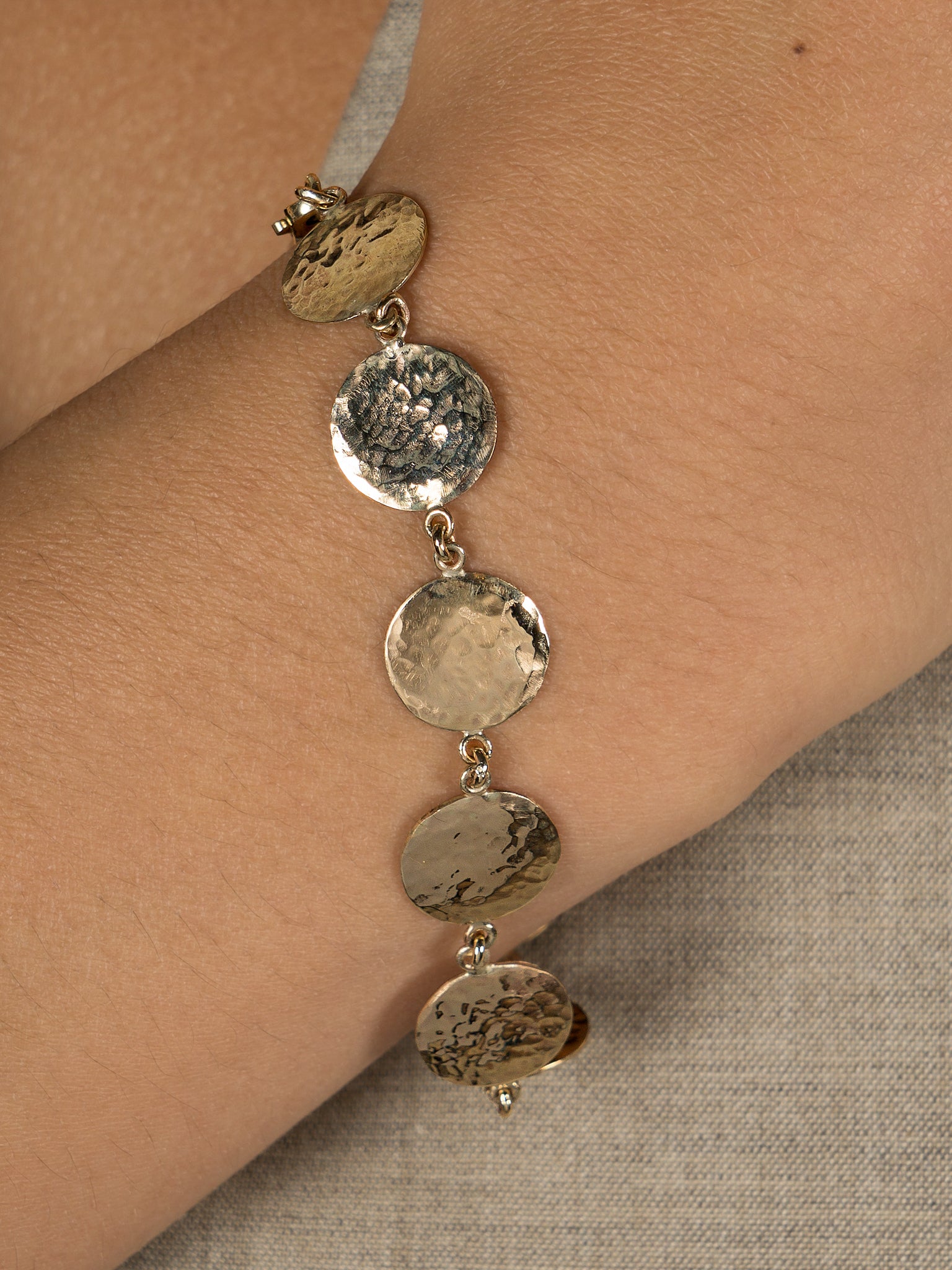Close up shot shows model wearing Lavey London's Solid 9ct Gold Hammered Disc Bracelet. 