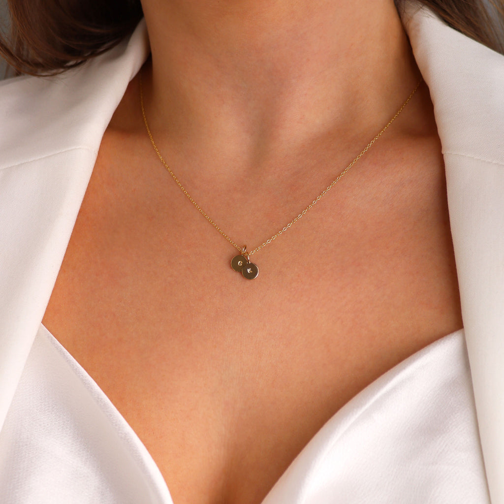 Gold mini disc pendant necklace with personalised engraving worn by model in white top and blazer