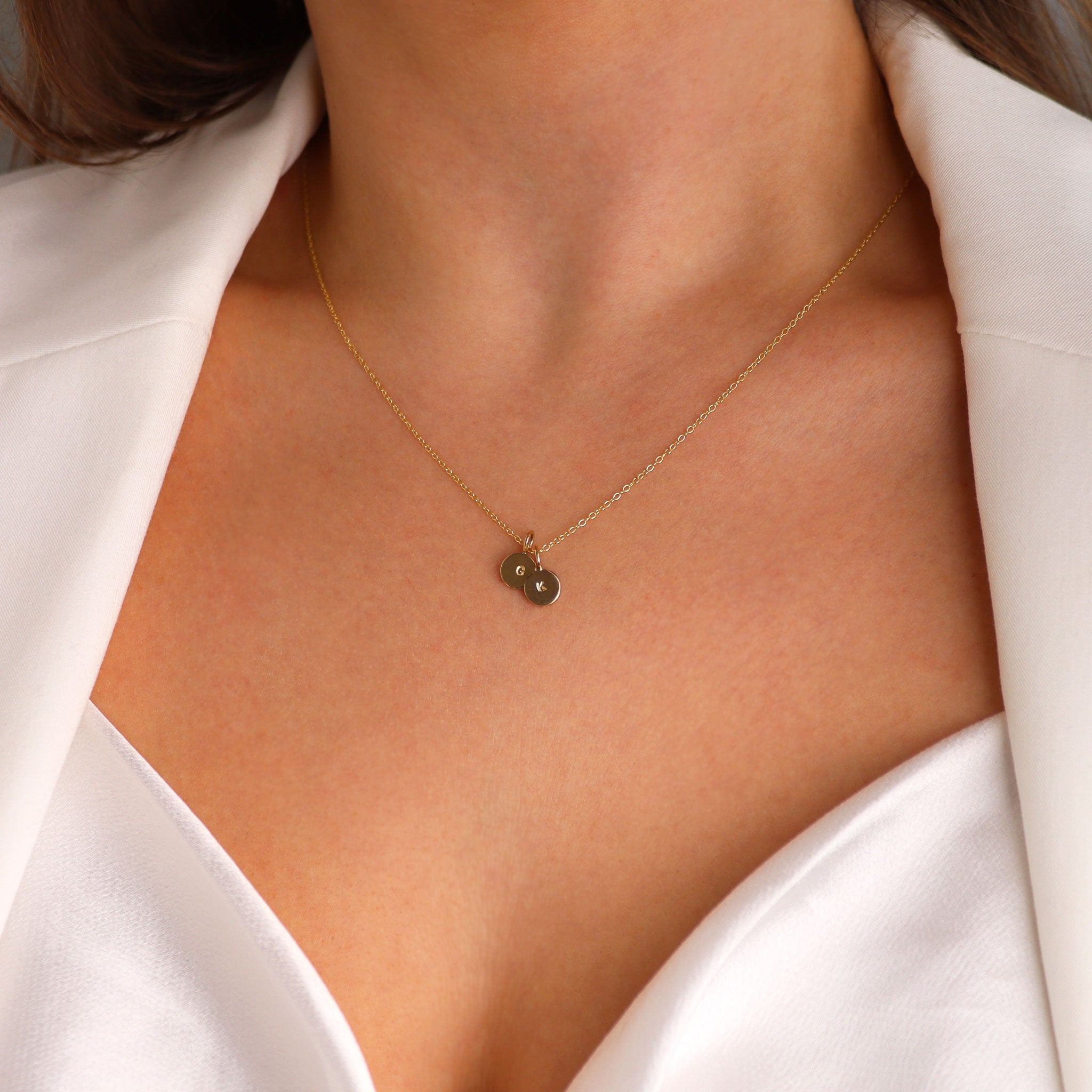 Gold mini disc pendant necklace with personalised engraving worn by model in white top and blazer