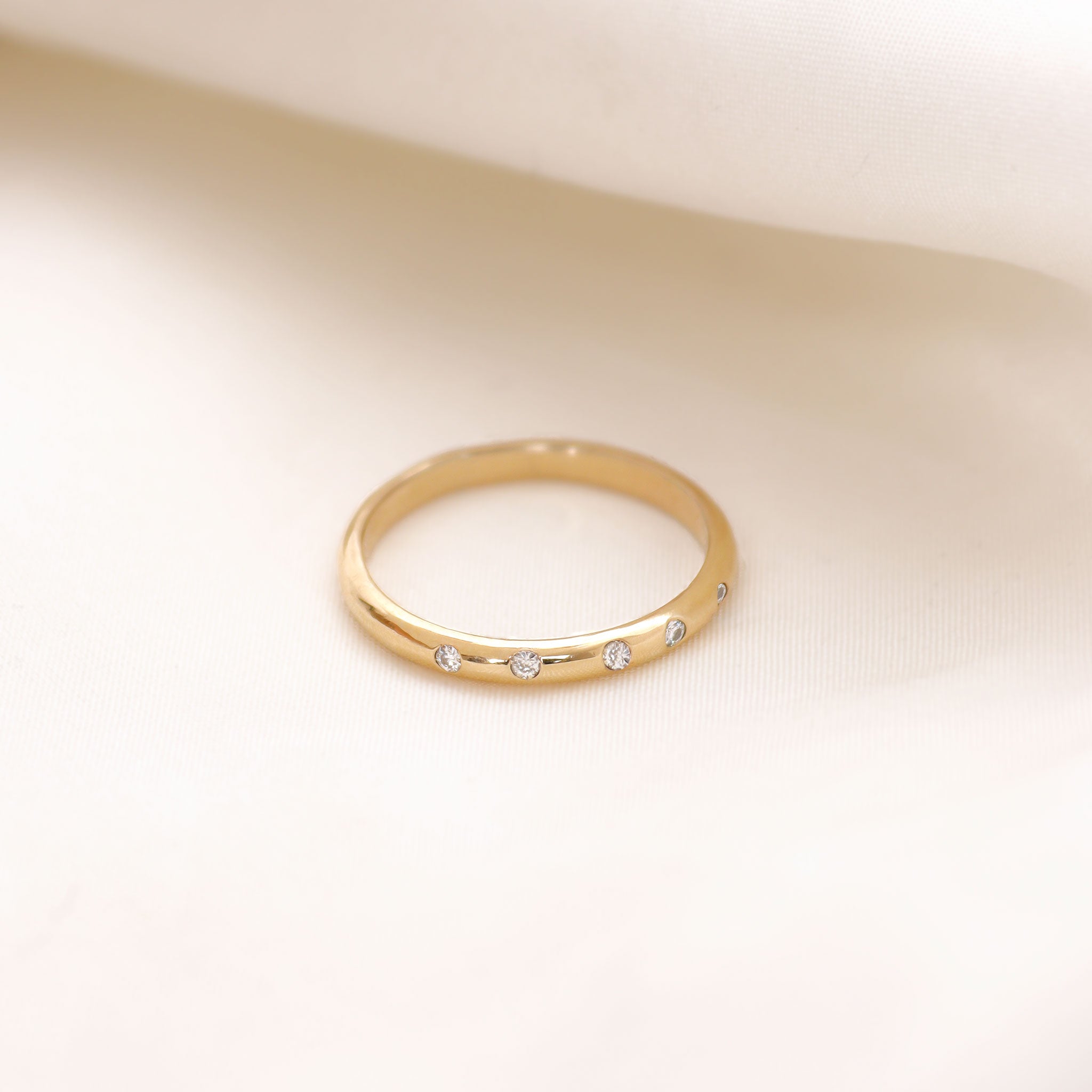 Lavey London's Solid Gold Flush Set Diamond Wedding Band Against A White Fabric Background